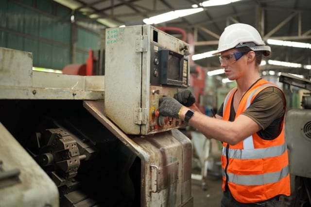 Portrait of Professional Heavy Industry Engineer / Worker Wearing Safety Uniform, Goggles and Hard Hat. In the Background Unfocused Large Industrial Factory